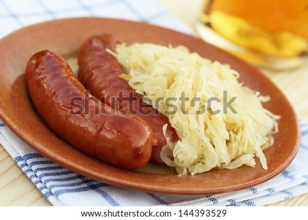 Plate with sausages and pickled cabbage. Detail of glass with beer.