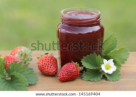 Glass with strawberry jam, strawberries and strawberry leaves and flower.