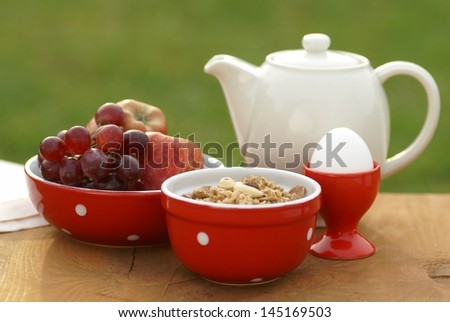 Bowl with cereal, egg, fruits and jug on a garden table.