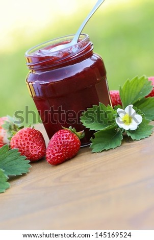 Glass with strawberry jam, strawberries and strawberry leaves and flower.