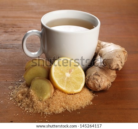 Cup of ginger tea and fresh ingredients - ginger, lemon and brown sugar.