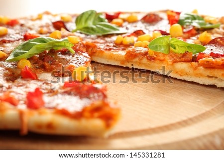 Pizza with salami, corn and herbs on wooden tray.