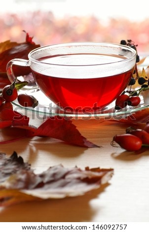 Cup of fruit rose-hip tea and autumn leaves and fruits on a table