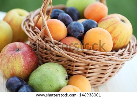 Basket filled with apples, pears, apricots and plums.