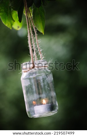 Jar with burning candle hanging on a tree.