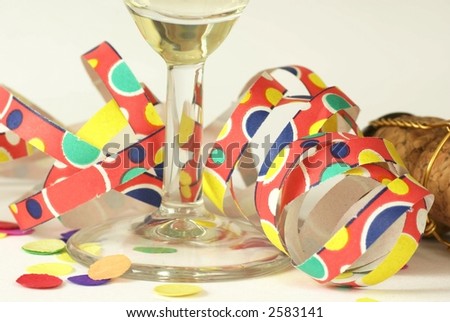 Detail of glass with champagne, curly ribbon, confetti and cork on white background