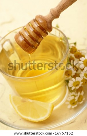 Herbal ea with lemon and honey. Chamomile on a saucer. Focus on wooden spoon with honey.