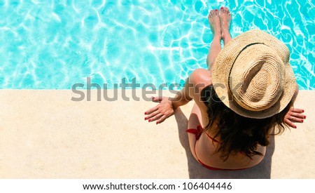 Woman sitting in a swimming pool with a sunhat
