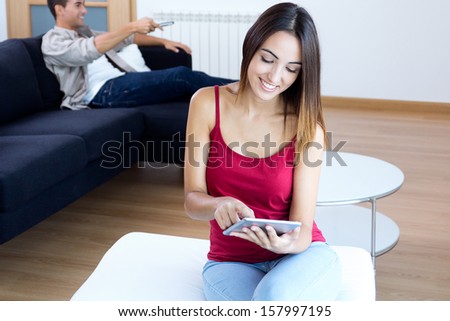 Pretty young woman using a digital tablet while her boyfriend is watching tv