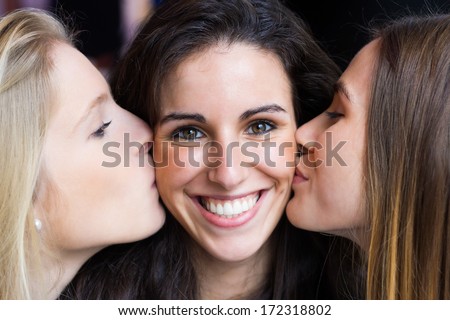 Portrait of cute smiling girl kissed on the cheeks by her friends.