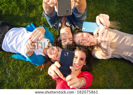 Outdoor portrait of group of friends taking photos with a smartphone in the park