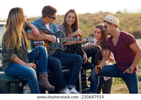 Outdoor portrait of group of friends playing guitar and drinking beer.