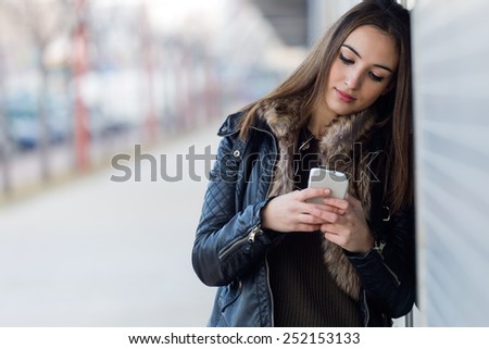 Outdoor portrait of young beautiful woman with mobile phone.