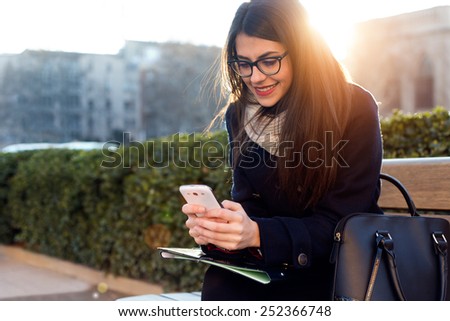 Outdoor portrait of young beautiful woman using her mobile phone.