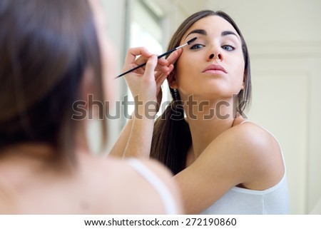 Portrait of beautiful young woman making make-up near mirror.