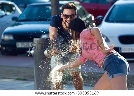 Outdoor portrait of two friends playing with a fountain in the street.