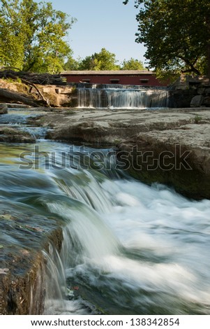 Cascading water downstream from red covered bridge