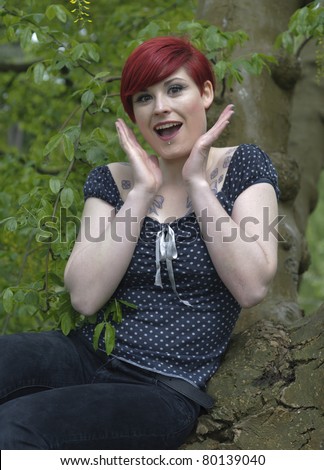 Outdoor portrait of a girl with red hair, piercing on lower lip, and tattoos on chest and shoulders, surprise  expression