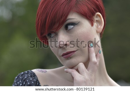 Portrait of a girl with red hair, piercing on lower lip, tattoos on shoulders and doubtful look