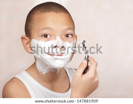 A young boy with no beard experiments with his father\'s shaving utensils.