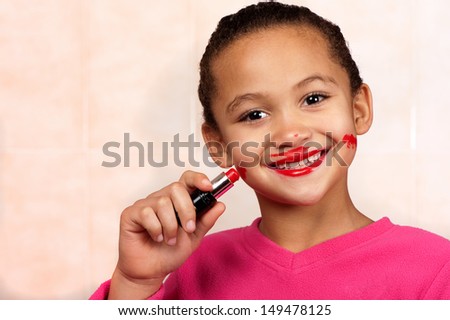 A smiling young girl applies lipstick in an unconventional manner.