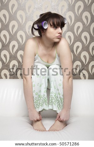 young adult girl with hair rollers sitting at white sofa and looking
