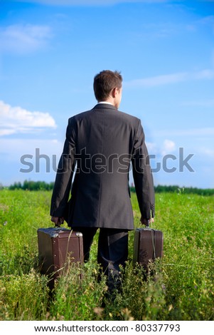 Parting with old two suitcases in his hands the businessman in the field, seen from behind