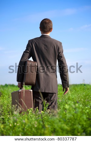 Parting with old two suitcases in his hands the businessman in the field, seen from behind