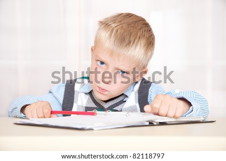 schoolboy sitting at a desk with a notebook and pencil and angry. portrait, close up