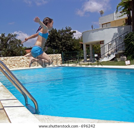 Young girl in blue bathing suit caught airborne while jumping into swimming pool