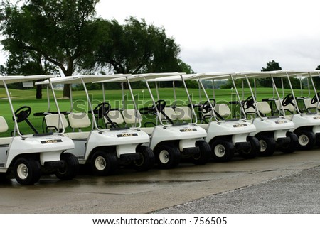 A photograph taken of golf carts parked in a row waiting for the rain to clear.