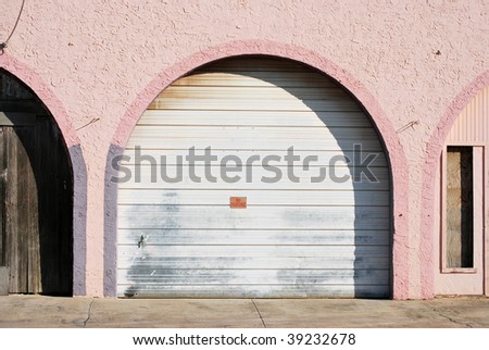 A photograph of a arched garage door with pink and purple walls in a street alley.
