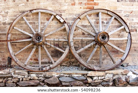 Two old-fashioned wood wagon wheels against a wall