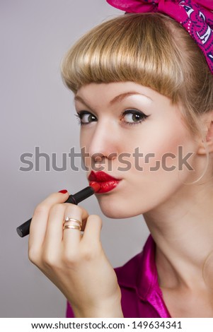 girl makes up lips with red lipstick on a gray background