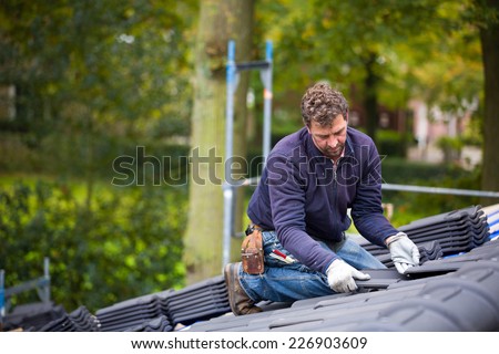 Male worker laying tiles on the roof while roofing a house near the city of Breda, Netherlands, Europe, in a traditional craftsman way
