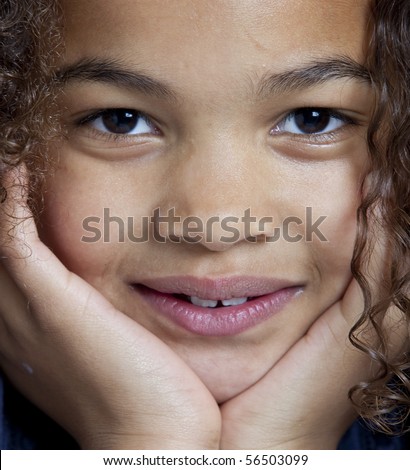 Little girl with frizzy hair is looking into the camera in a close up portrait of her face, with the hands supporting her chin which leads to a symmetrical composition