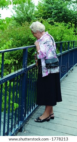 A happy 85 year old senior lady on a bridge in a park looking down into the river