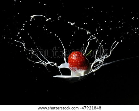Strawberry creating a splash as it is dropped onto a spoon filled with cream