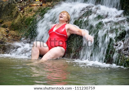 Adult woman in red swimsuit enjoying a waterfall in a mountain river (Russia, Sochi National Park)