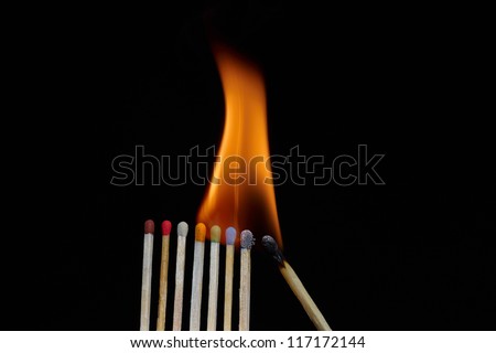 A line of multi color safety matches showing burnt out matches on the right, through burning matches, ignition, and unused ones on the left.