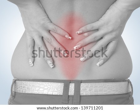 Acute pain in a woman back. Female from behind holding hand to spot of back pain. Concept photo with read spot indicating location of the pain. Isolation on a white background.