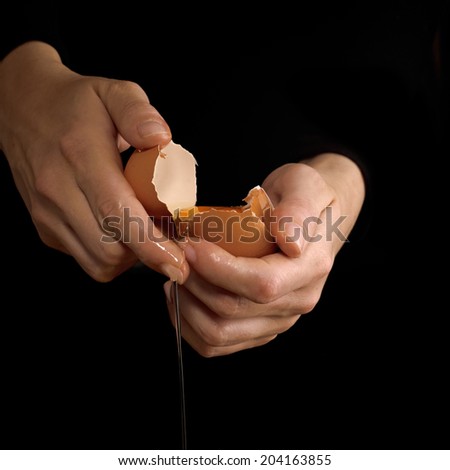 Hands breaking an egg. Egg Yolk dripping, falling, on black background.