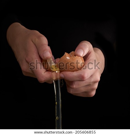 Hands breaking an egg. Egg Yolk dripping, falling, on black background.