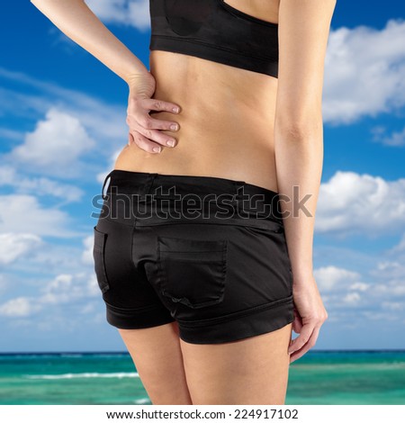 Back pain. Athletic woman in black sportswear standing and rubbing the muscles of her lower back, cropped torso.