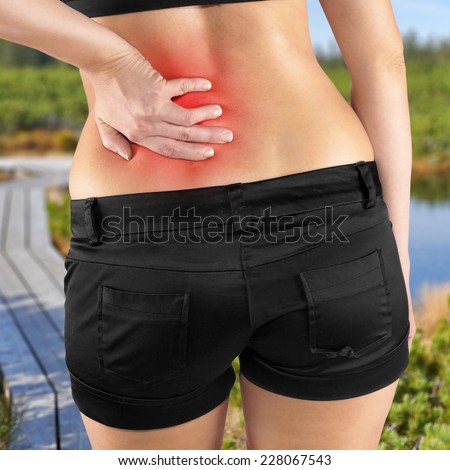 Back pain. Athletic woman in black sportswear standing and rubbing the muscles of her lower back, cropped torso portrait.Autumn Park Backgroun