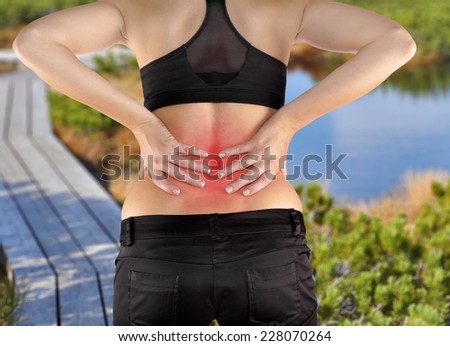 Back pain. Athletic woman in black sportswear standing and rubbing the muscles of her lower back, cropped torso portrait.Autumn Park Backgroun