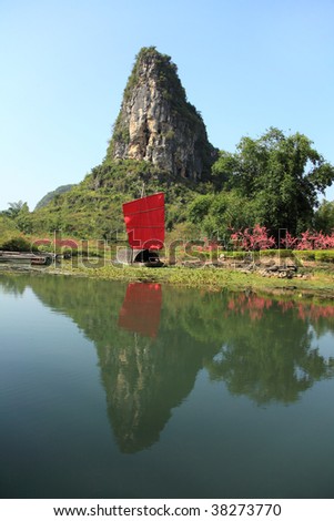 A karst mountain and bamboo boat perfectly reflected in a river in Southern China