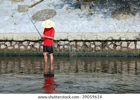 A Chinese fisherman with straw hat and red shirt on a riverbank