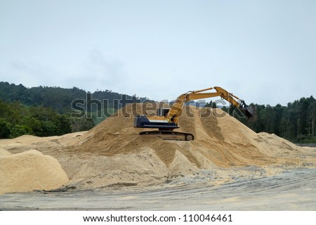 an excavator atop a sand hill in an open sand-mine in a jungle clearing