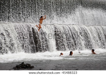 BALI - JANUARY 16: Children jump off the spillway and enjoy a morning swim at the dam in Ubud  January 16, 2010 in Bali, Indonesia.